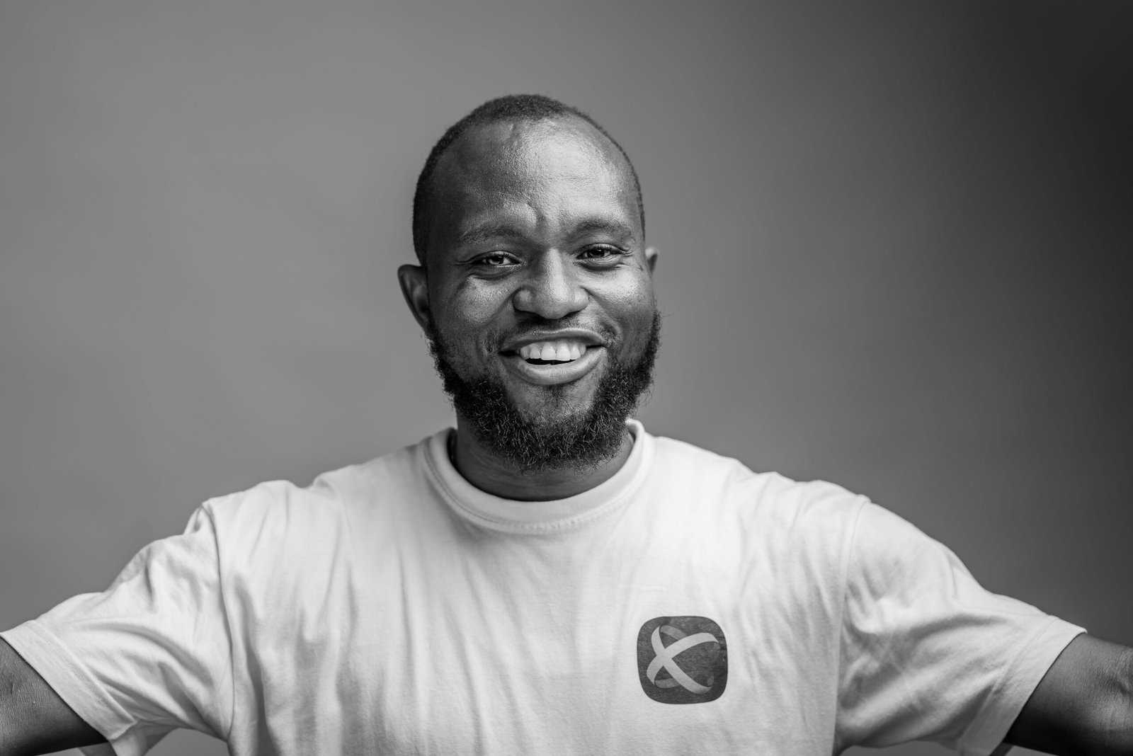 Black and white studio portrait of a smiling man in a casual t-shirt, arms open.